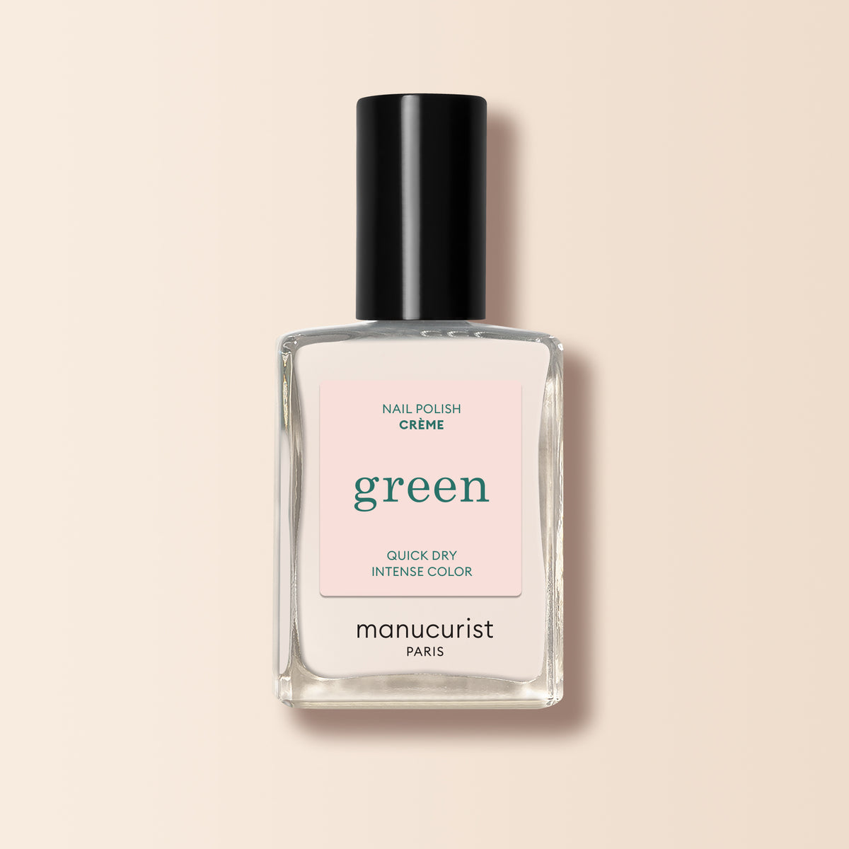 A clear Manucurist bottle from the Green range with a black cap and a pale pink “green” label displays the Crème shade, a milky off-white nail polish, against a light beige background.
