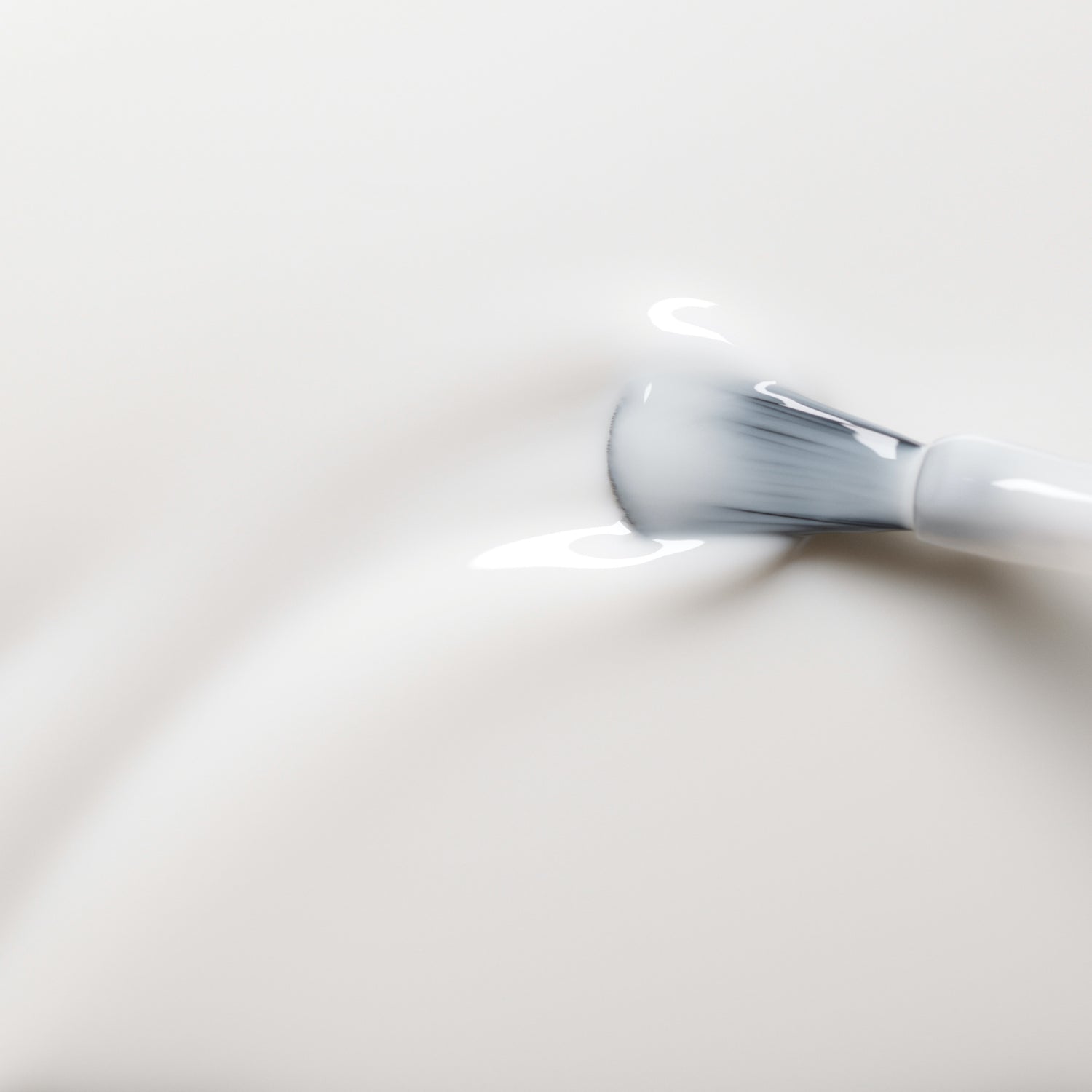 A makeup brush with white bristles gently swirls through the smooth, creamy Milky white OLD gel nail polish by Manucurist-test on a light background, highlighting its easy-to-remove formula.