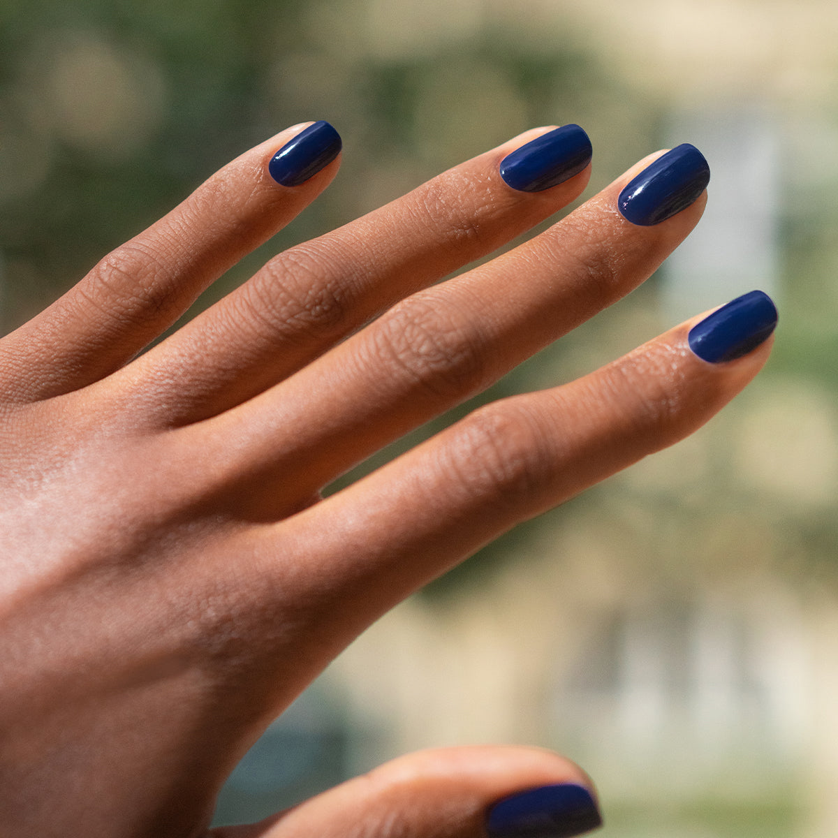 A hand with medium brown skin and neatly manicured nails painted in Manucurist&