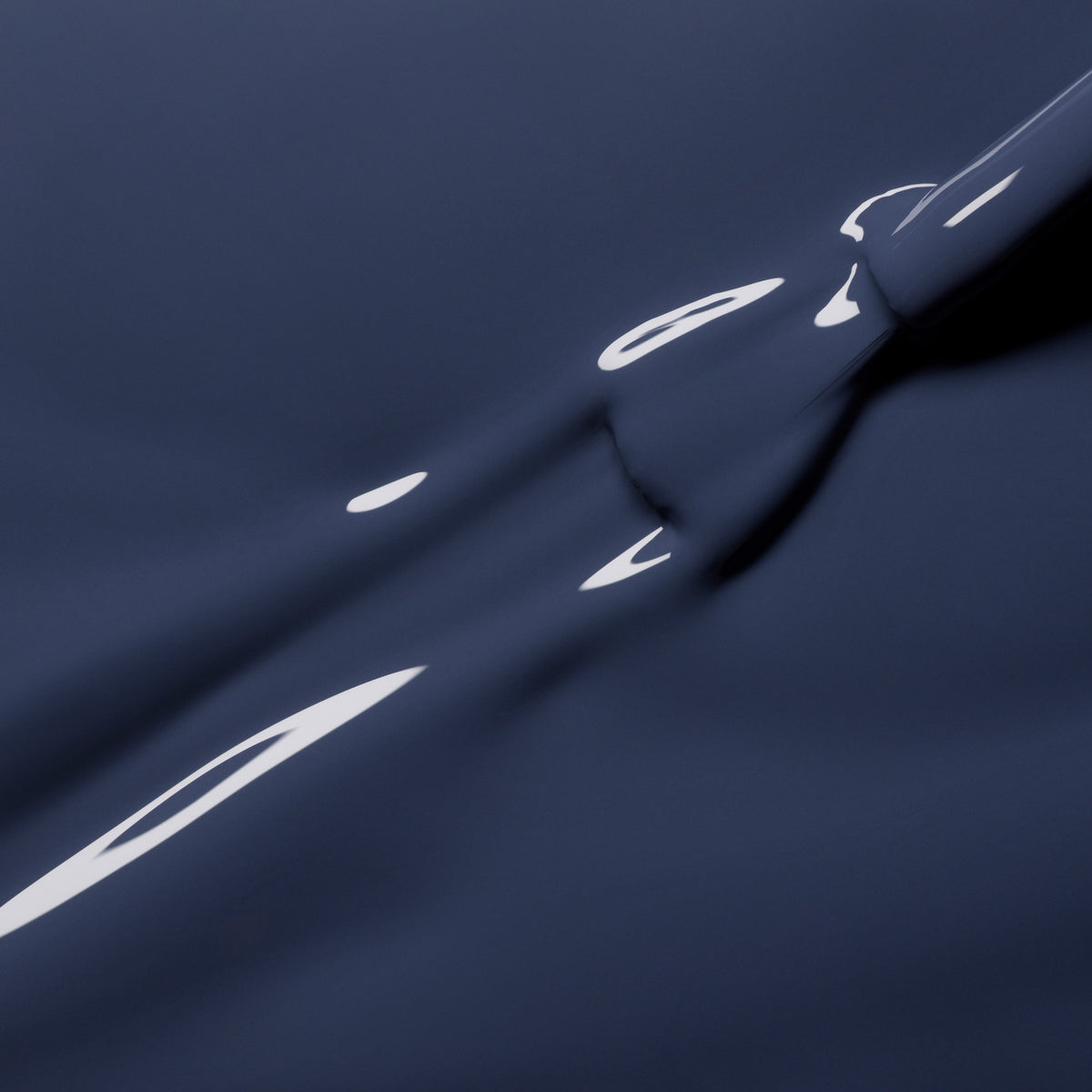 Poppy Seed by Manucurist features a smooth, dark blue surface with glossy, reflective streaks and curved lines, reminiscent of liquid or satin fabric—evoking the luminous sheen of bluish grey nail polish under light.