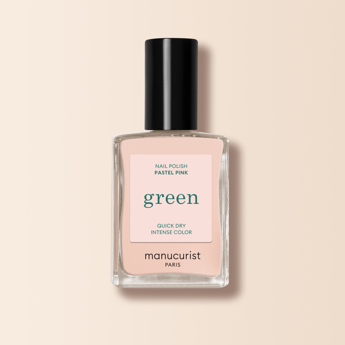 A clear glass bottle of Manucurist Pastel Pink nail polish with a black cap and beige undertones sits against a pale peach background. The label reads "Nail Polish Pastel Pink, Quick Dry Intense Color, manucurist PARIS.