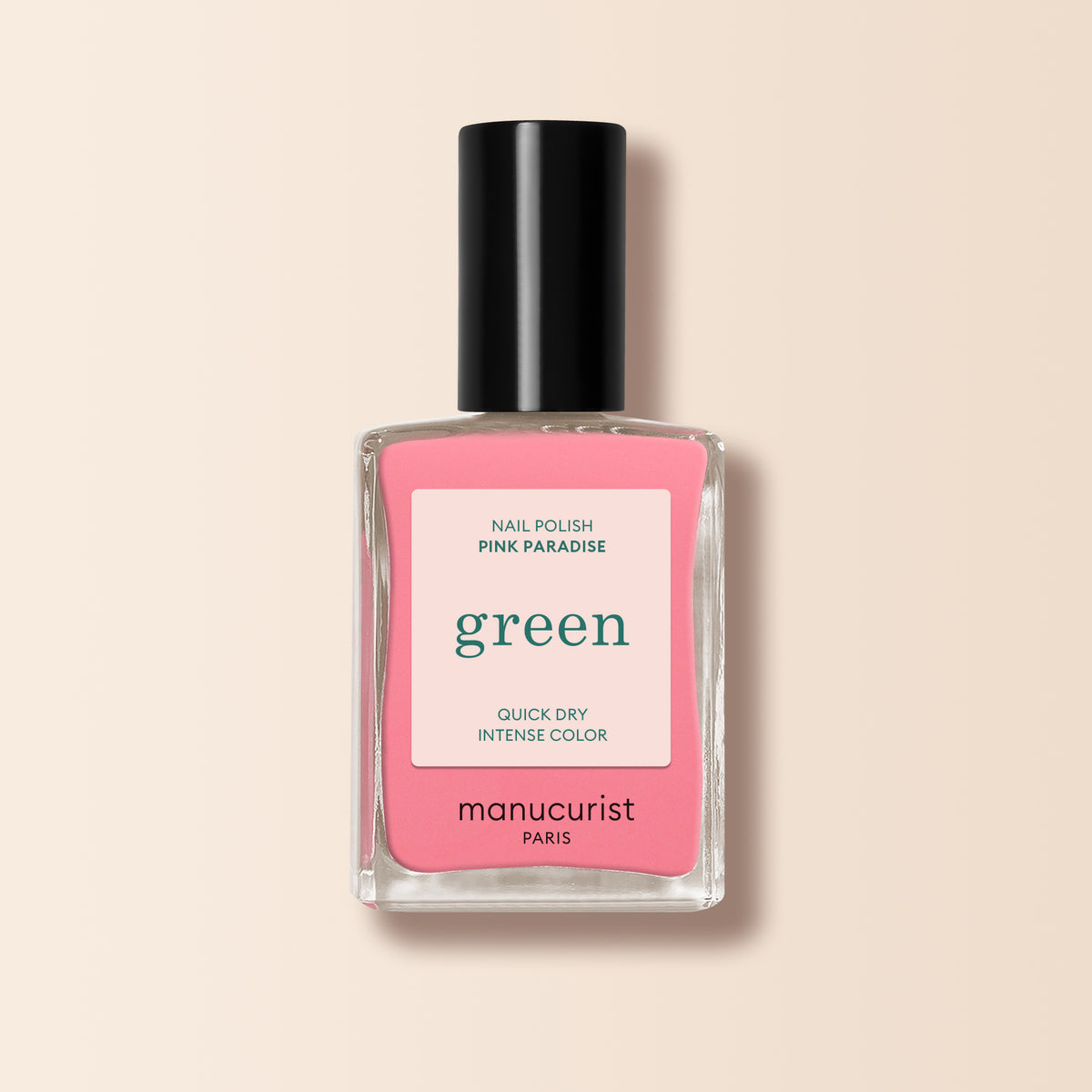A bottle of Manucurist Pink Paradise nail polish, featuring a pink label and black cap with “quick dry intense color” text, is displayed against a beige background.