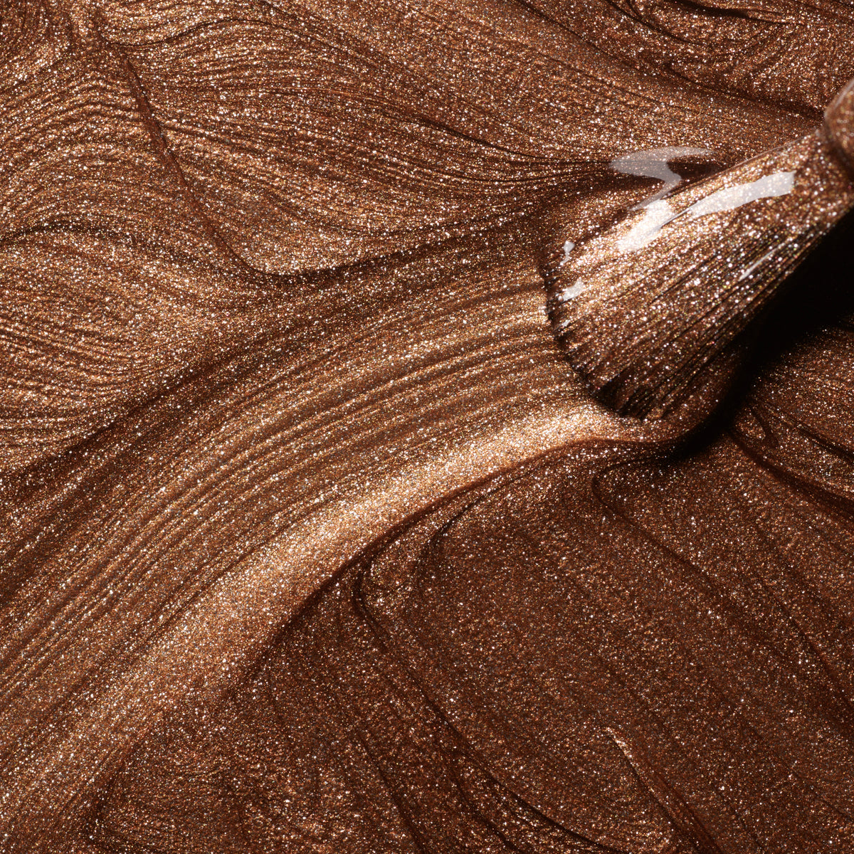Close-up of a brush applying Manucurist Bronzé nail polish, creating swirling, reflective copper lines and textured patterns with fine brown glitter.