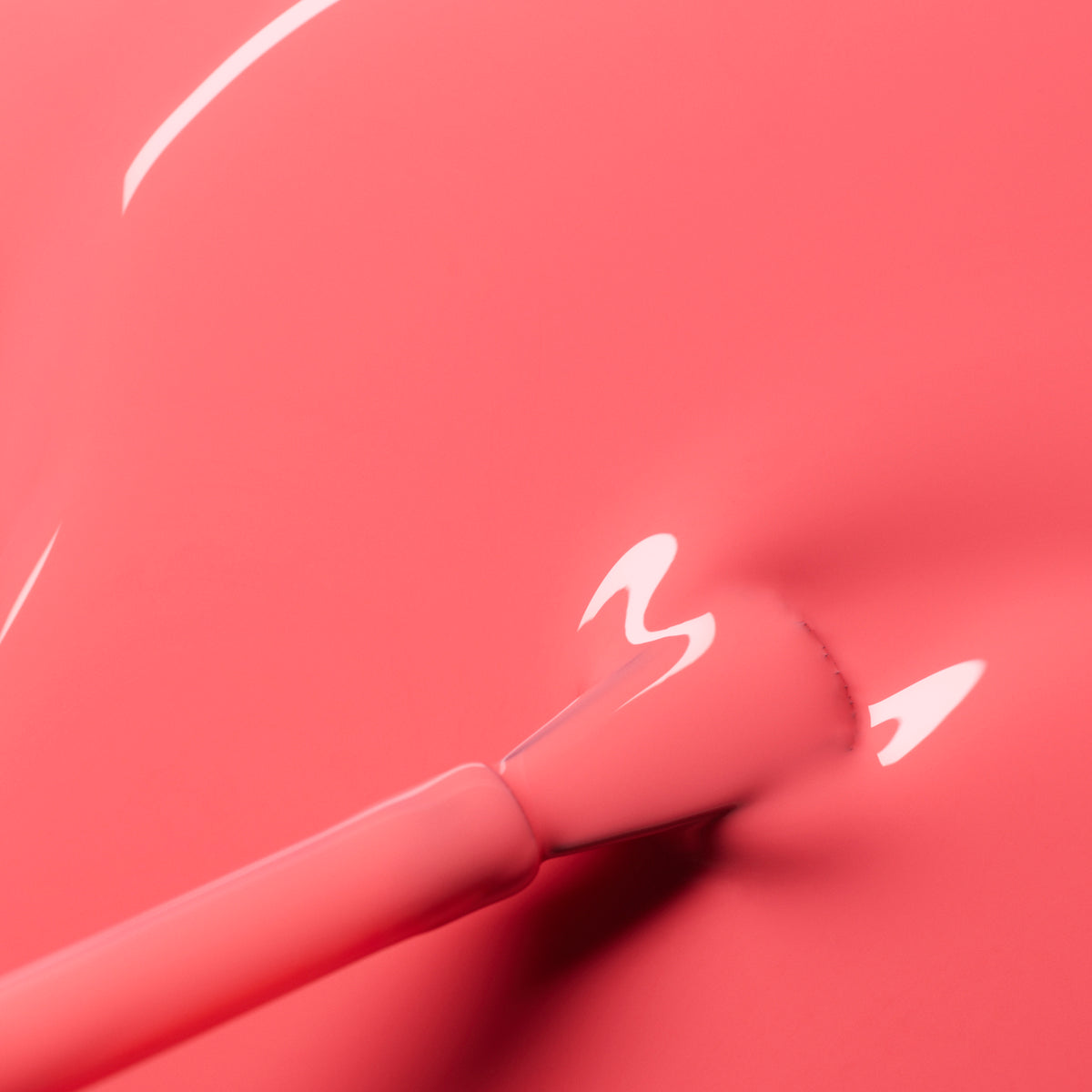 A close-up of a brush applying Capucine by Manucurist, a glossy coral pink polish with a smooth, shiny texture and reflective highlights.