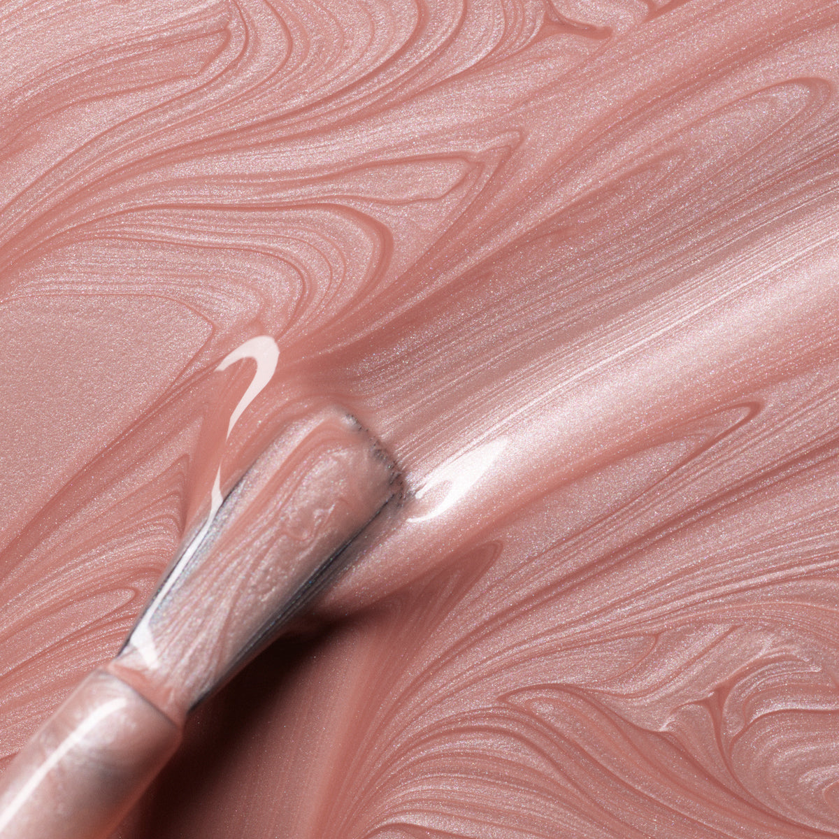A close-up of a brush spreading Manucurist Carnation polish in smooth, swirling patterns. This Green™ range shade features a glossy, pearly pink beige finish with visible brush stroke textures.