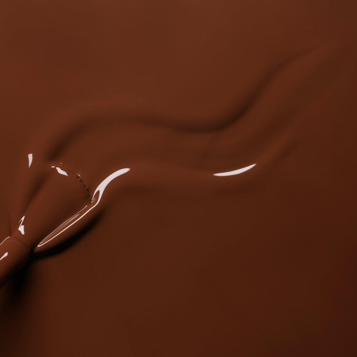 A close-up of smooth, glossy melted chocolate being swirled with a utensil, its flowing wave patterns mirroring the rich, warm brown shade of Manucurist’s Chestnut nail polish.