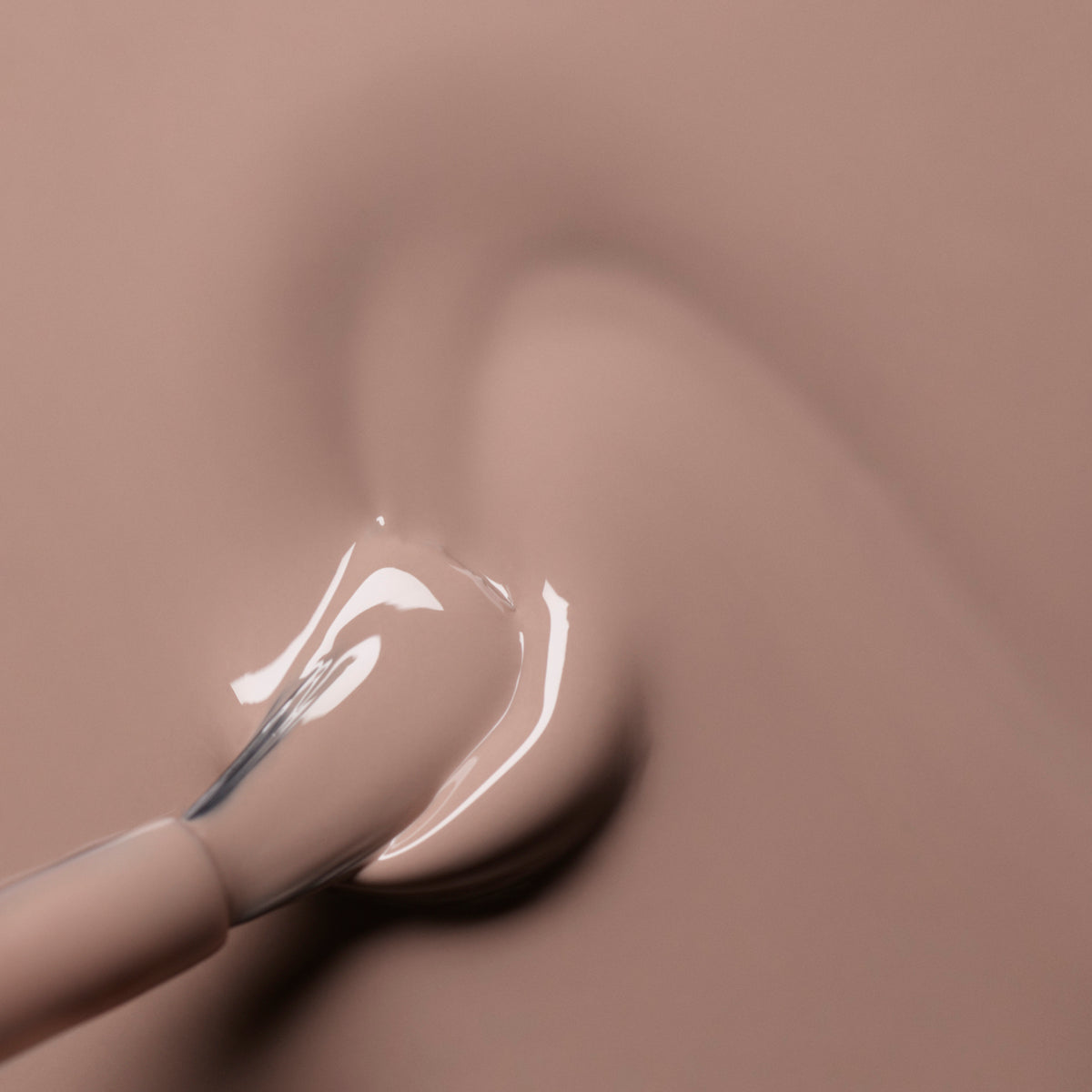 A close-up of a brush applies Dove Beige nail polish from Manucurist onto a smooth surface, creating a soft swirl pattern. Both the background and the Green™ polish feature the same elegant beige-pink hue.