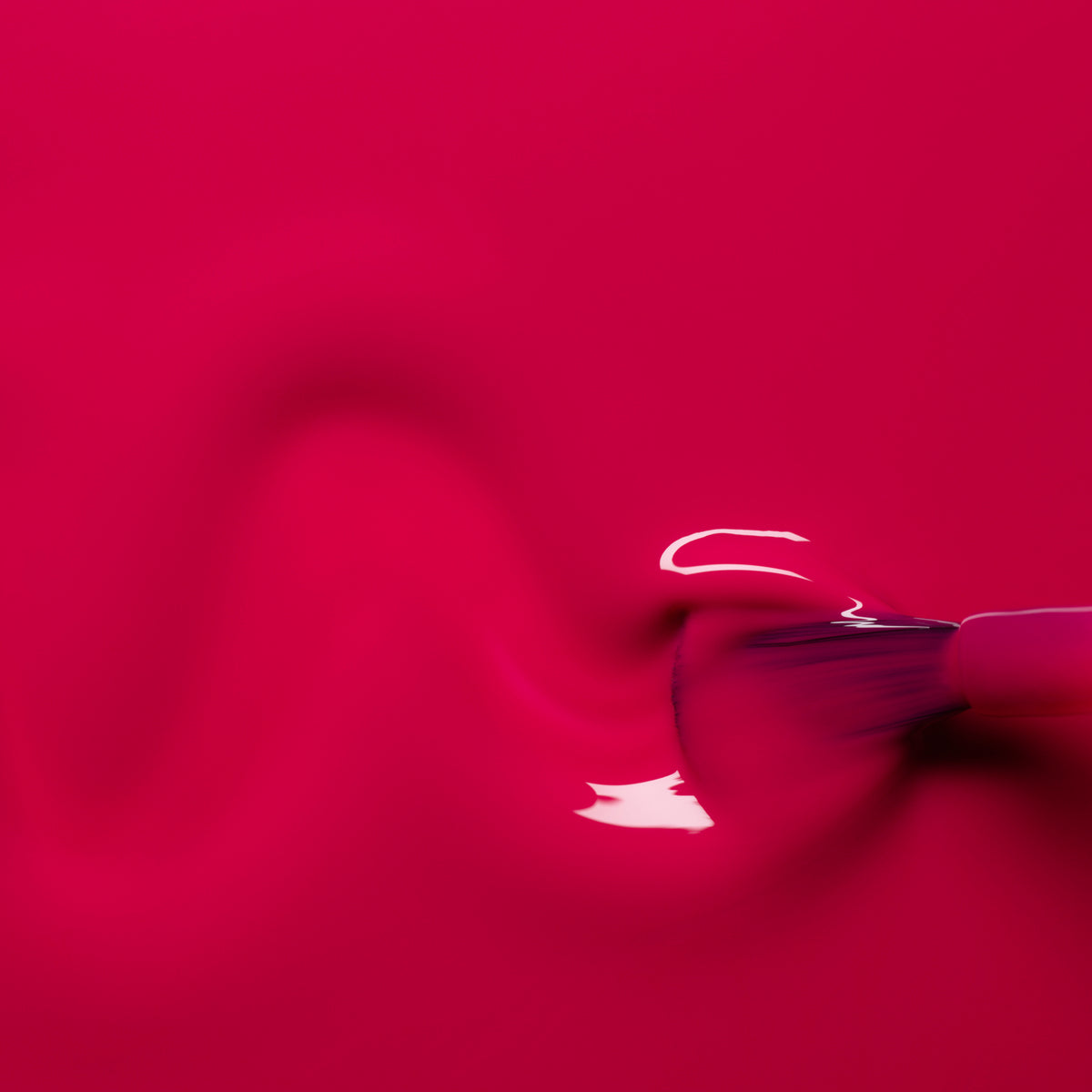 A close-up of a brush spreading Fuchsia nail polish in a wavy pattern across a smooth surface, revealing a glossy, reflective finish from Manucurist’s Green™ range.