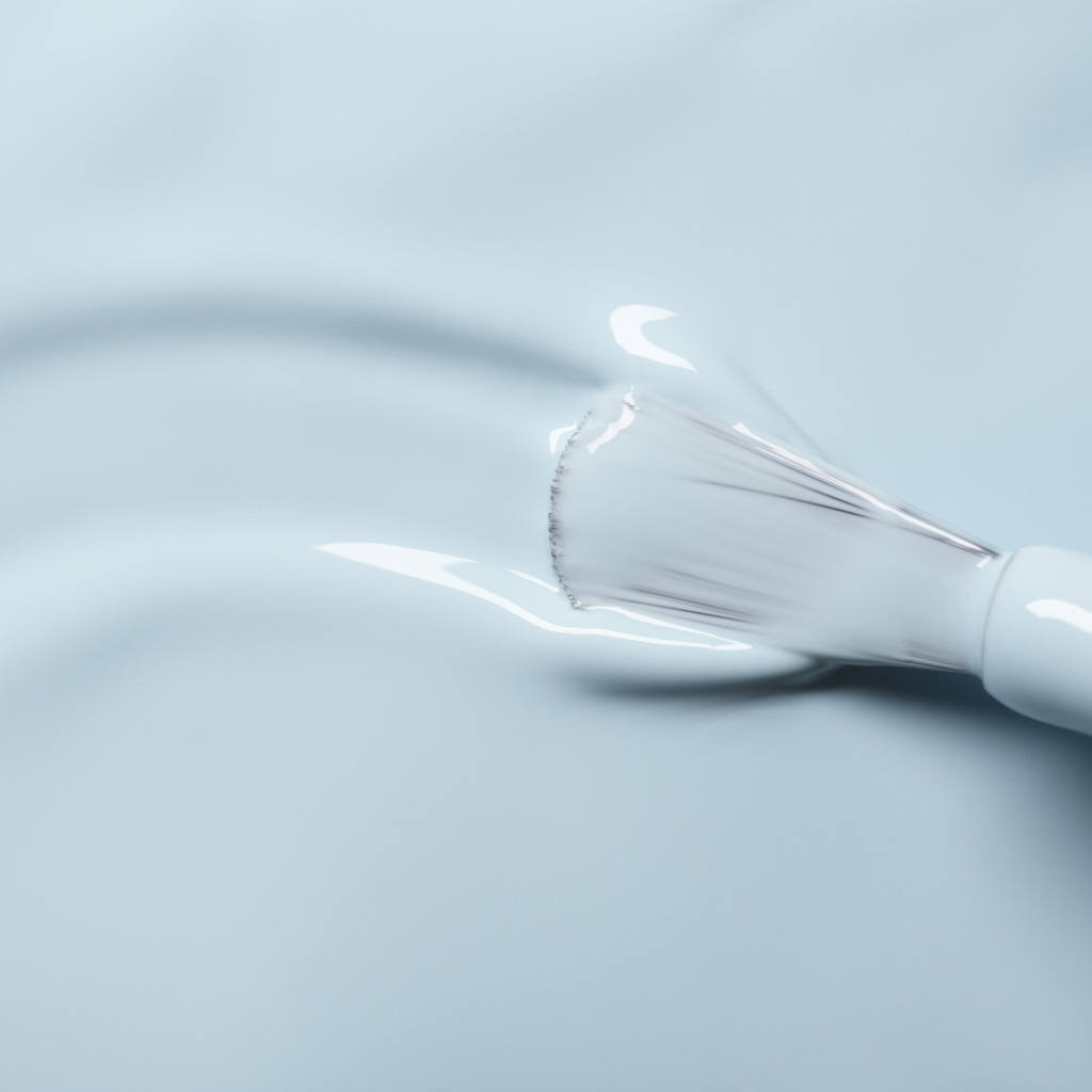 A close-up of a brush applying Manucurist’s Light Blue nail polish across a smooth surface.