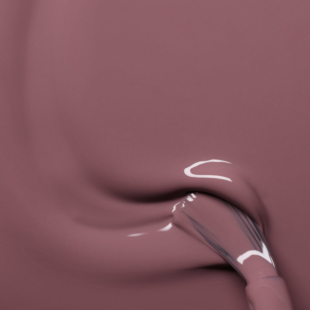 A glossy brush applies Manucurist’s Rose Mountbatten, a pinky taupe nail polish, in smooth, swirling strokes on a flat surface.