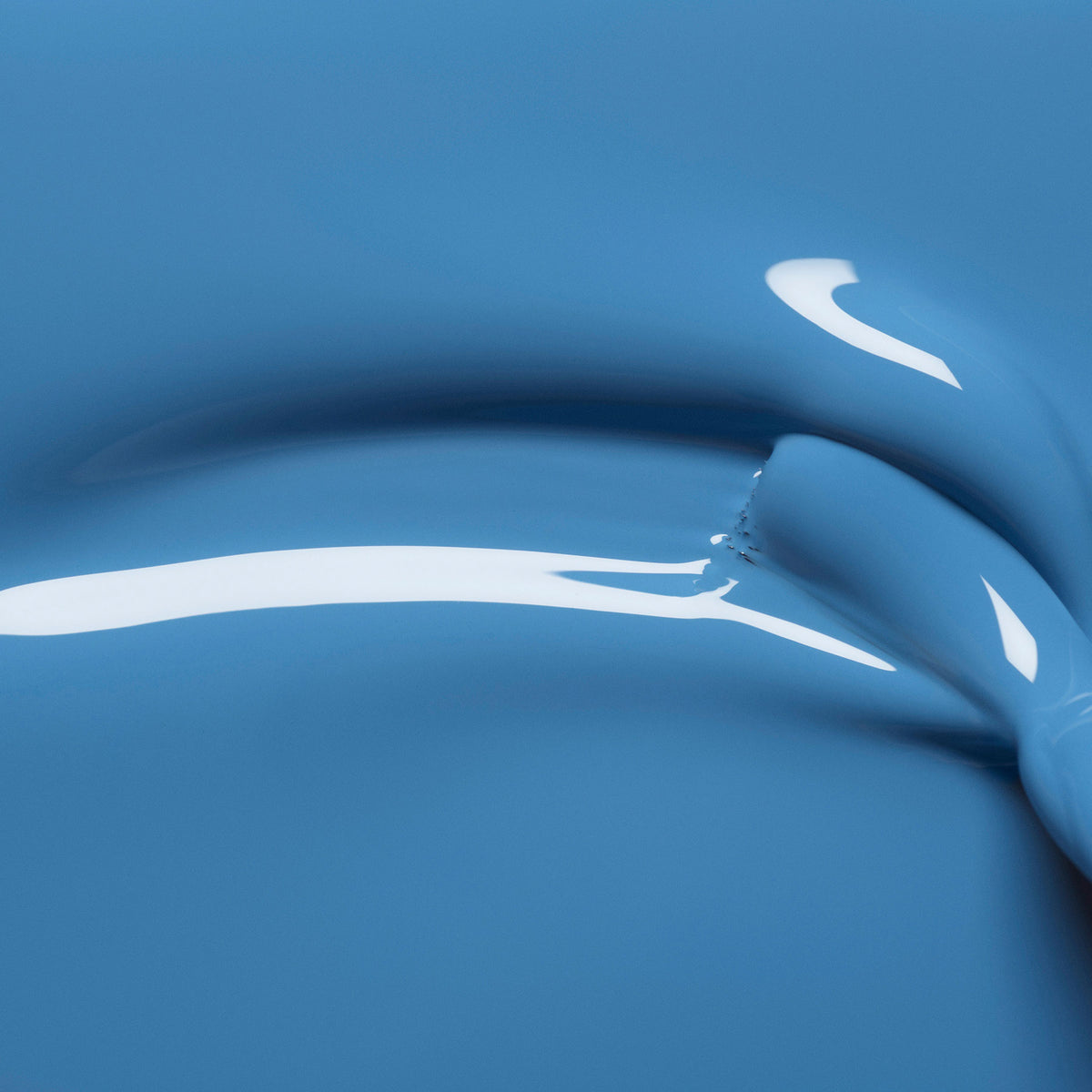 Close-up of smooth, shiny Manucurist Saphir blue paint featuring curved ridges and jewel-toned reflections on its surface.