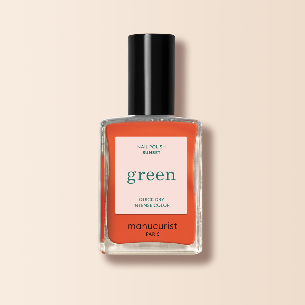 A bottle of Manucurist Sunset nail polish in vibrant orange from the Green™ range, with a black cap and a label reading "green, quick dry intense color," rests against a light beige background.