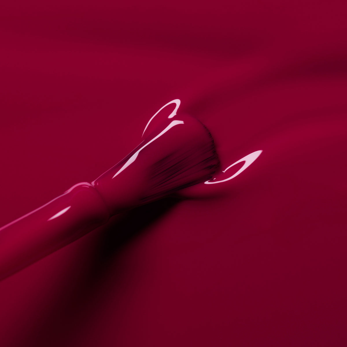 A close-up of the Manucurist Violeta brush applying glossy, burgundy-purple polish on a smooth surface. The shiny finish creates striking reflective highlights.