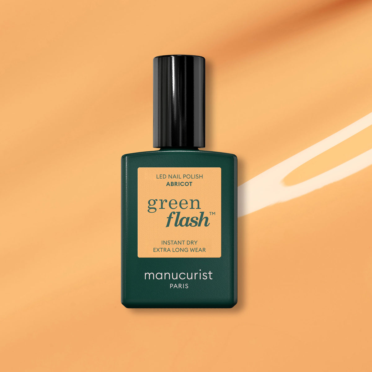 A bottle of Manucurist Abricot Green Flash gel polish, with a dark green cap and label, is displayed against a pastel orange background accented by a white streak.