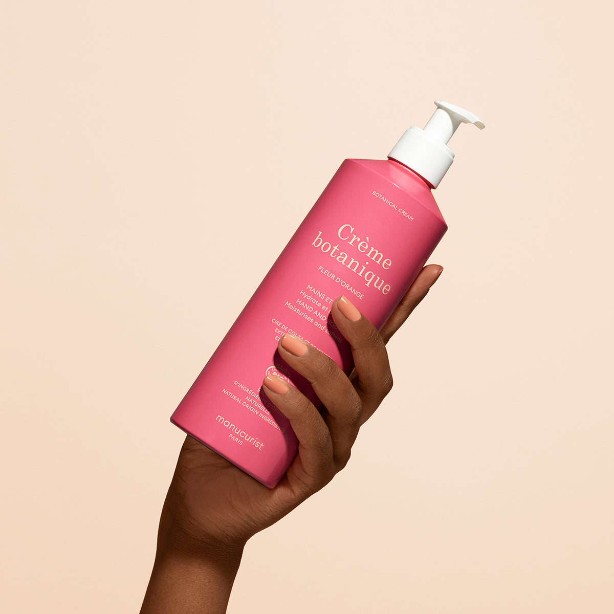 A hand with neatly manicured nails holds a pink pump bottle labeled Manucurist Fleur d&