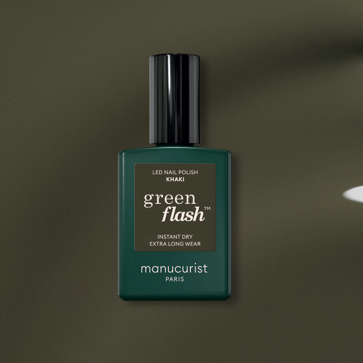 A bottle of Manucurist Khaki gel polish with a black cap is displayed on a muted khaki background. The label features instant dry and extra long wear benefits.