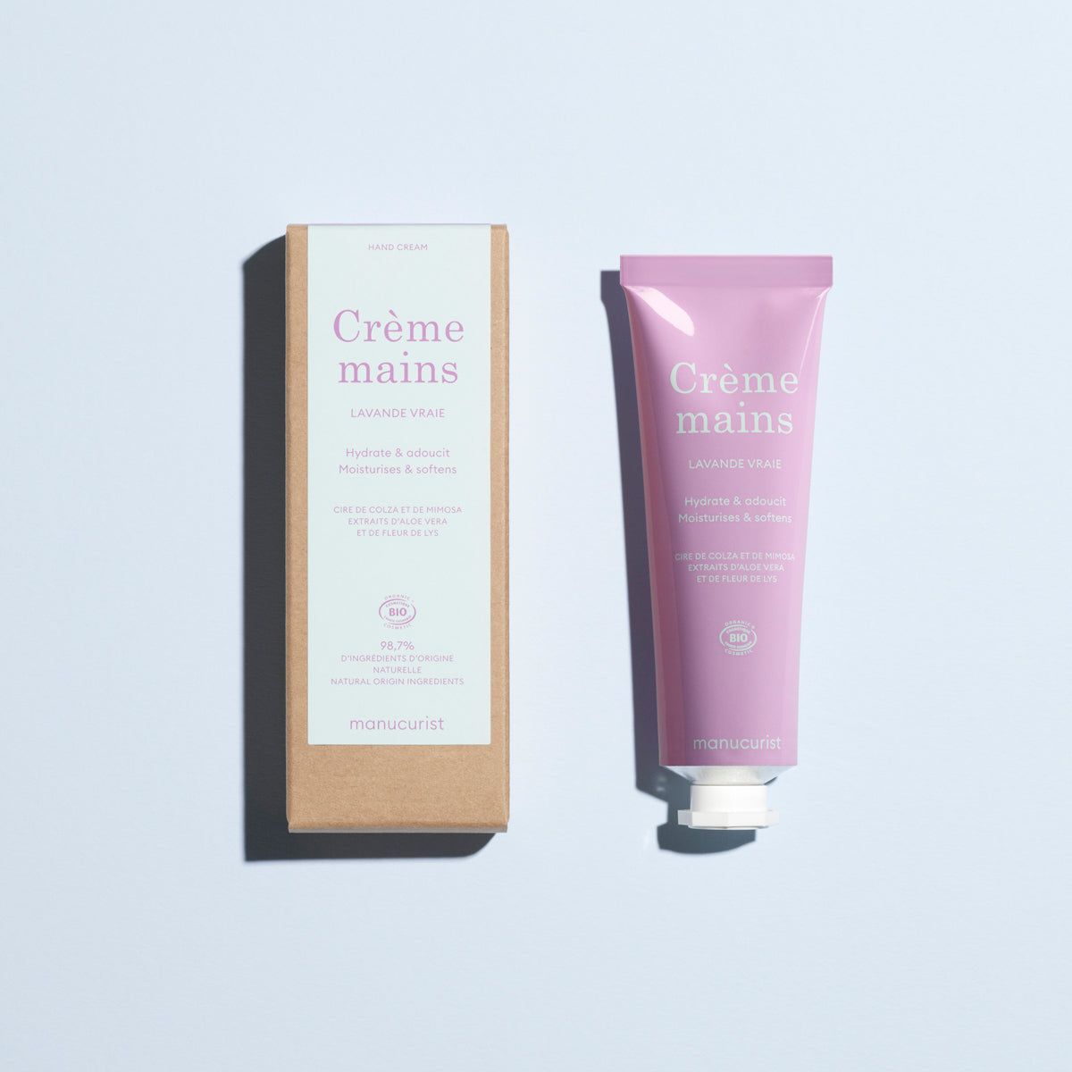 A lavender tube of Manucurist Lavande Vraie Hand Cream - Cosmos Organic is next to its brown box on a light blue background. Both feature French branding and product details.