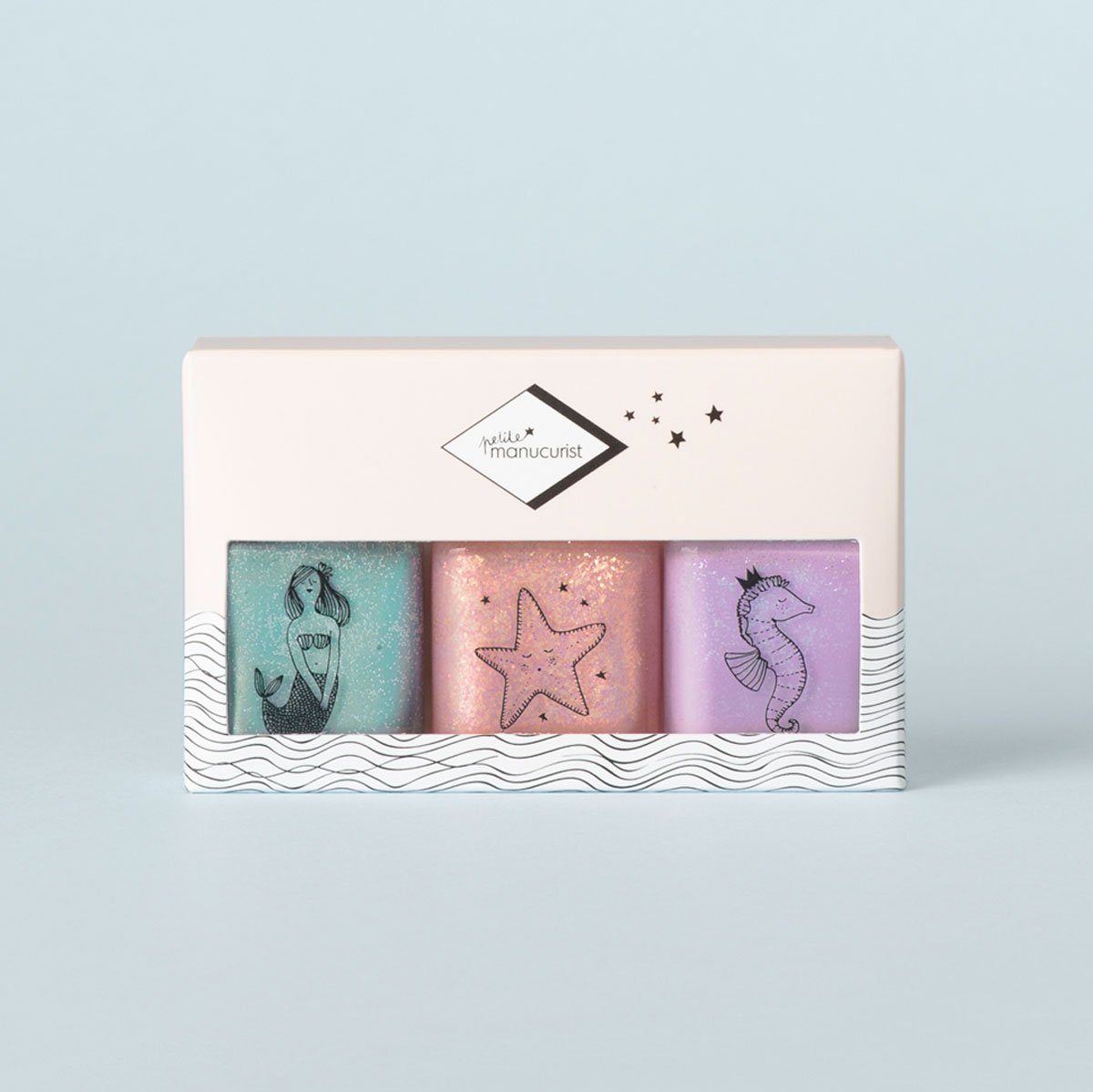The Bonnie Stella Janis set by Manucurist includes three pastel kids nail polishes: teal with a mermaid, pink with a starfish, and lavender with a seahorse, all in safe bottles and packaged in a box with a white wavy design.