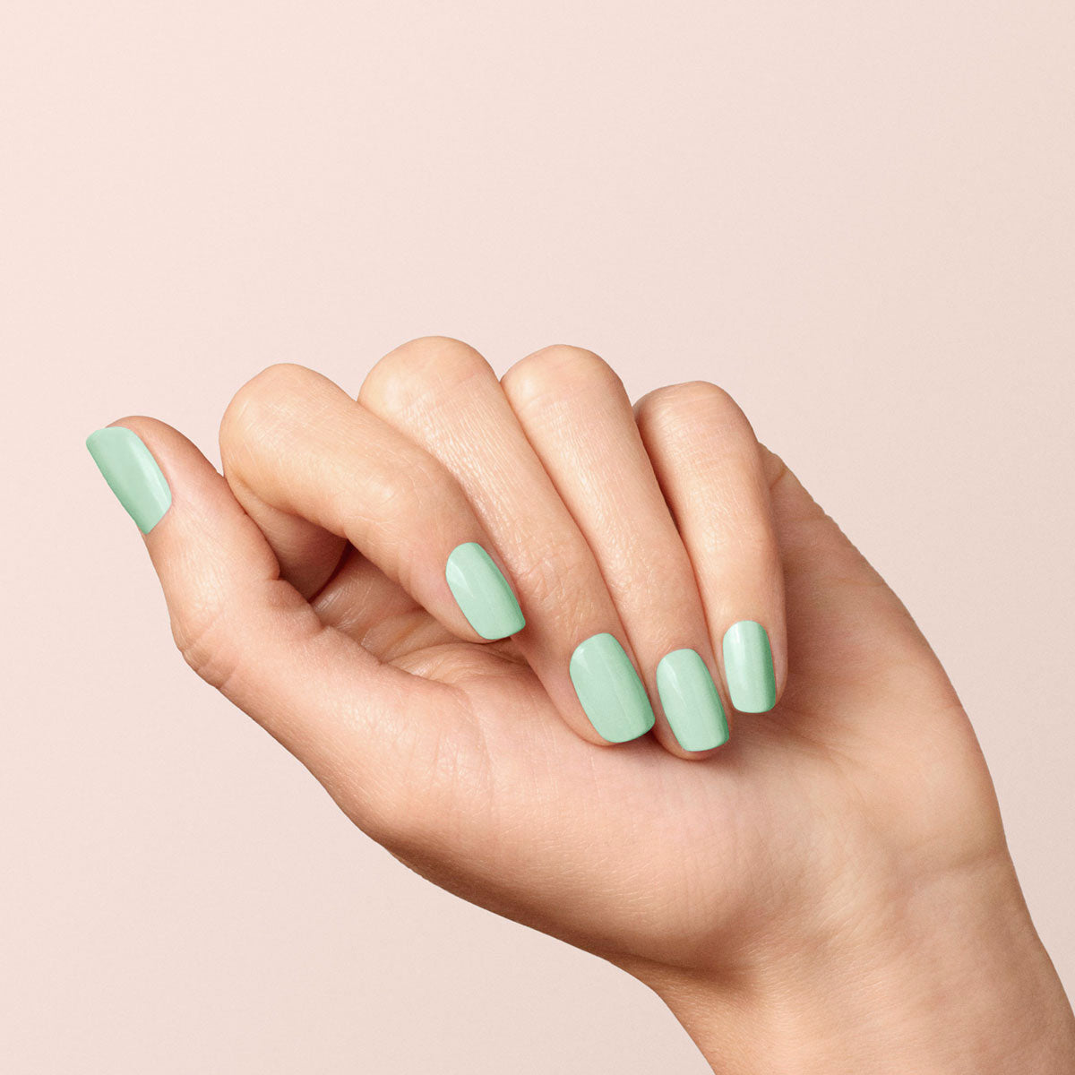 A hand with light skin tone is shown against a pale background, nails neatly manicured and painted with Manucurist&