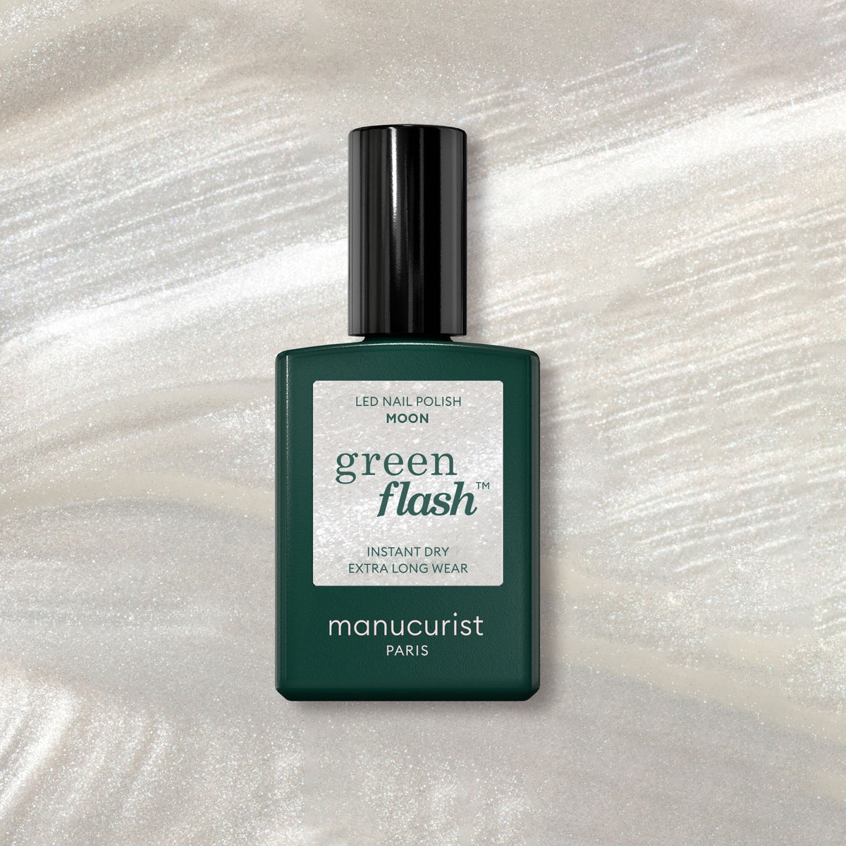 A bottle of Manucurist gel polish in the shade Moon rests on a shimmering marble surface. The dark green bottle, glossy black cap, and white label stand out against pearly highlights.