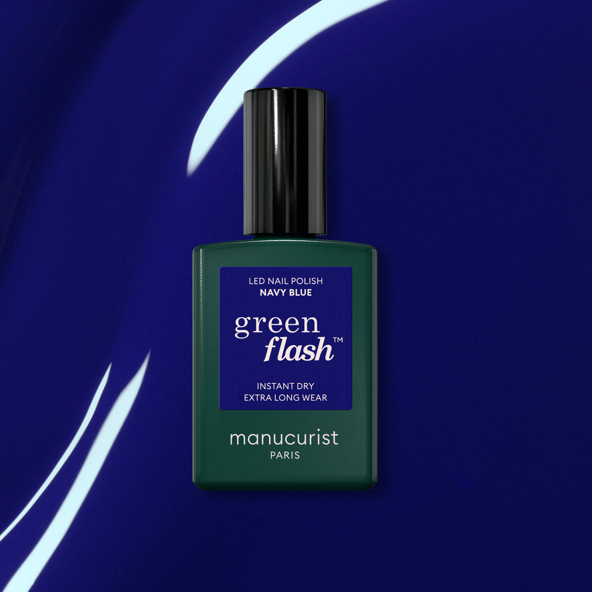 A bottle of Manucurist Navy Blue gel polish rests on a glossy dark blue surface with curved light reflections.