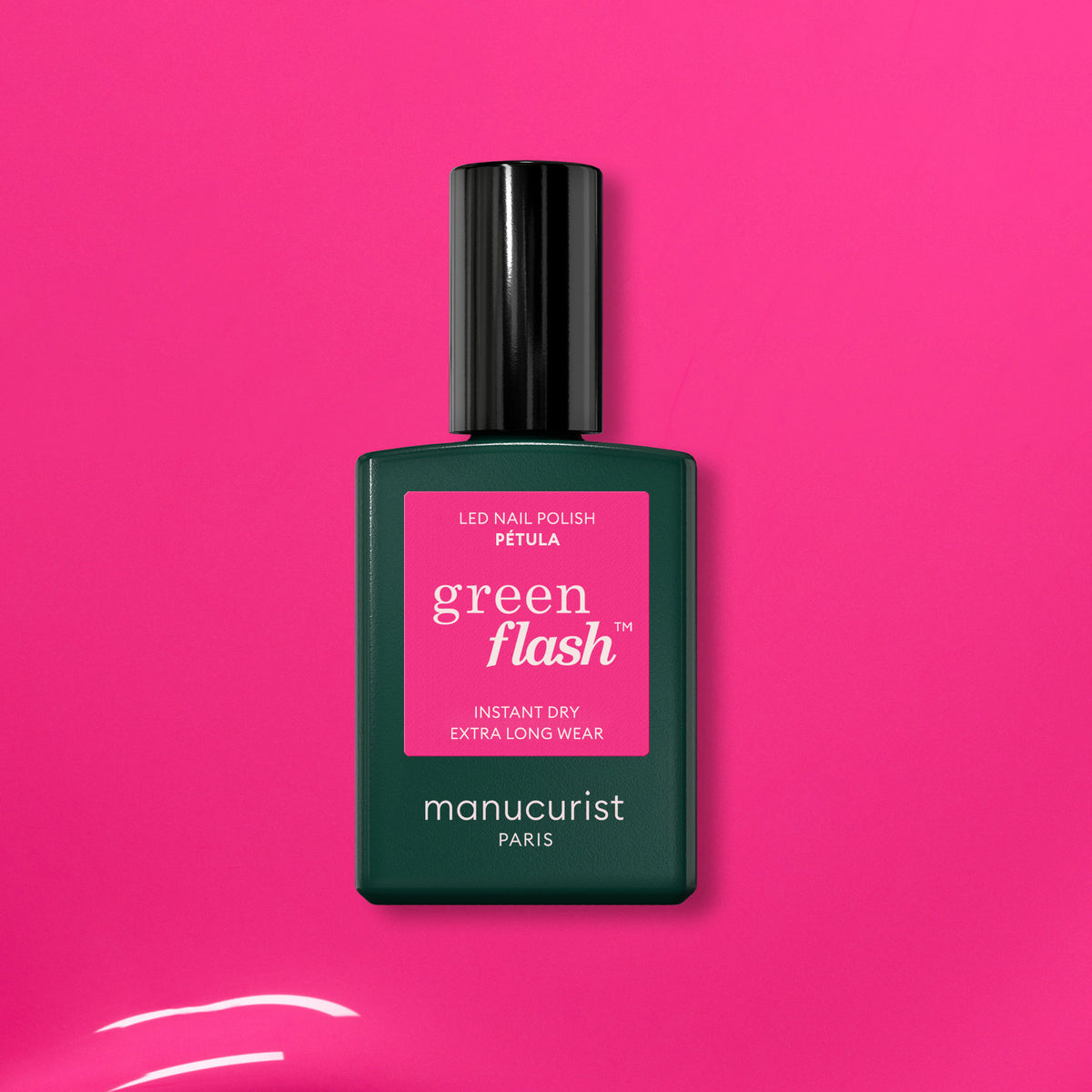 A bottle of Manucurist Green Flash LED nail polish in the shade Pétula rests on a bright pink surface, featuring a label that states instant dry and extra long wear.
