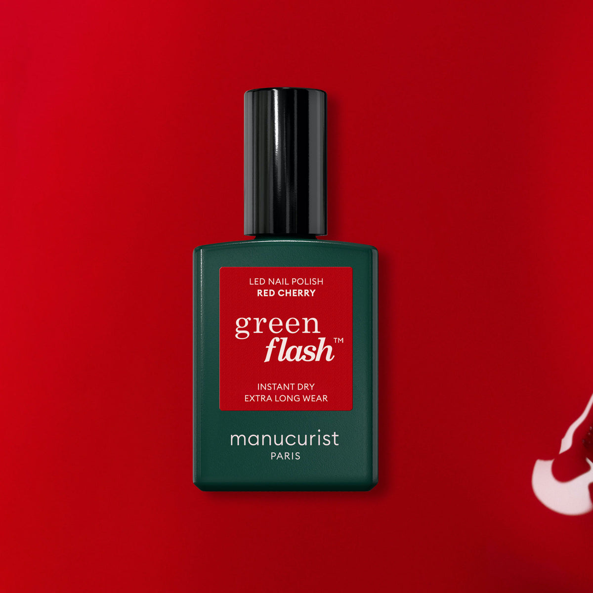 A bottle of Manucurist Red Cherry Green Flash gel polish stands centered on a red background, featuring a black cap and a red label with white text—an elegant showcase of this classic shade.